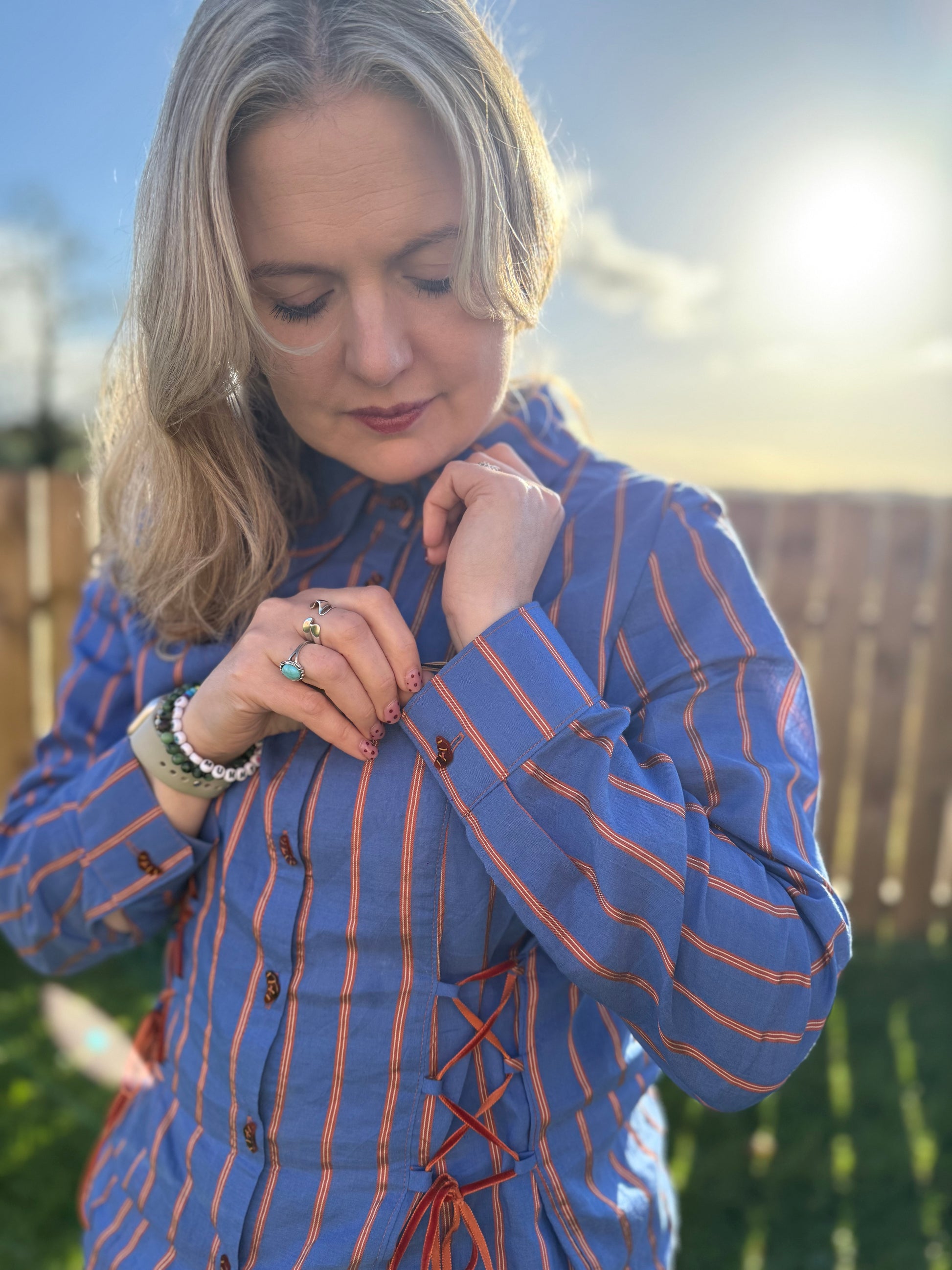 Woman wearing a blue and orange striped shirt outdoors with a blurred background